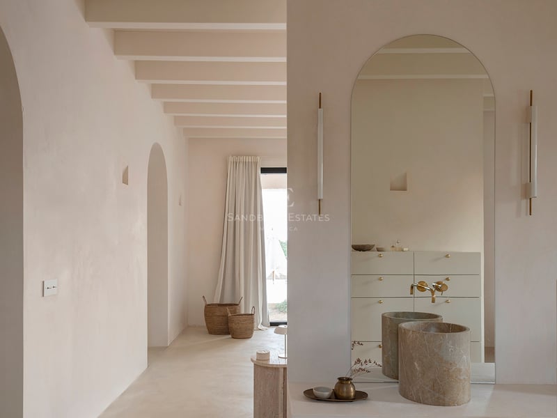 Minimalist bathroom with arched mirror, cylindrical stone sink, and exposed ceiling beams in sand tones.