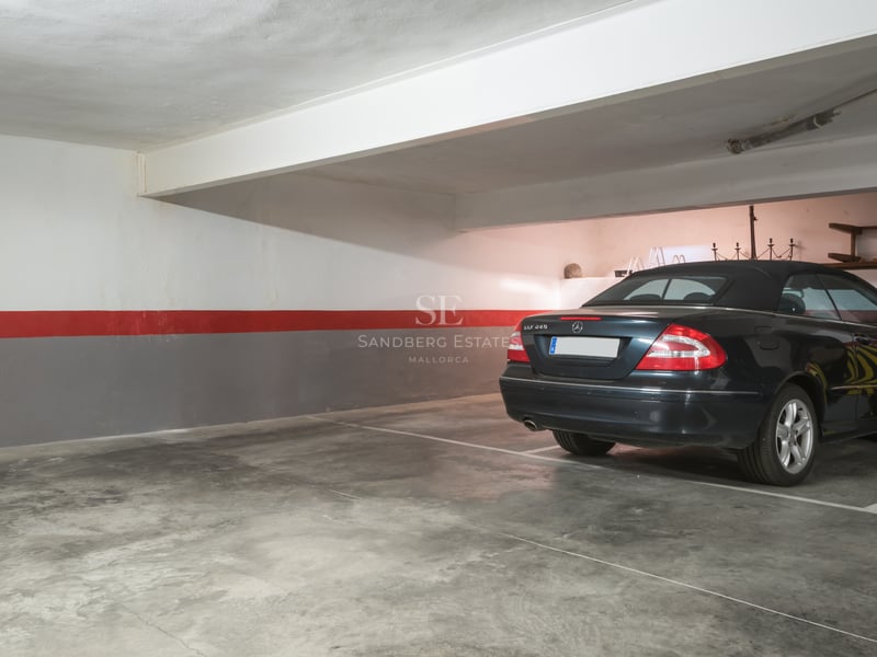Voiture noire stationnée dans un grand parking souterrain avec sol en béton poli et murs balisés.
