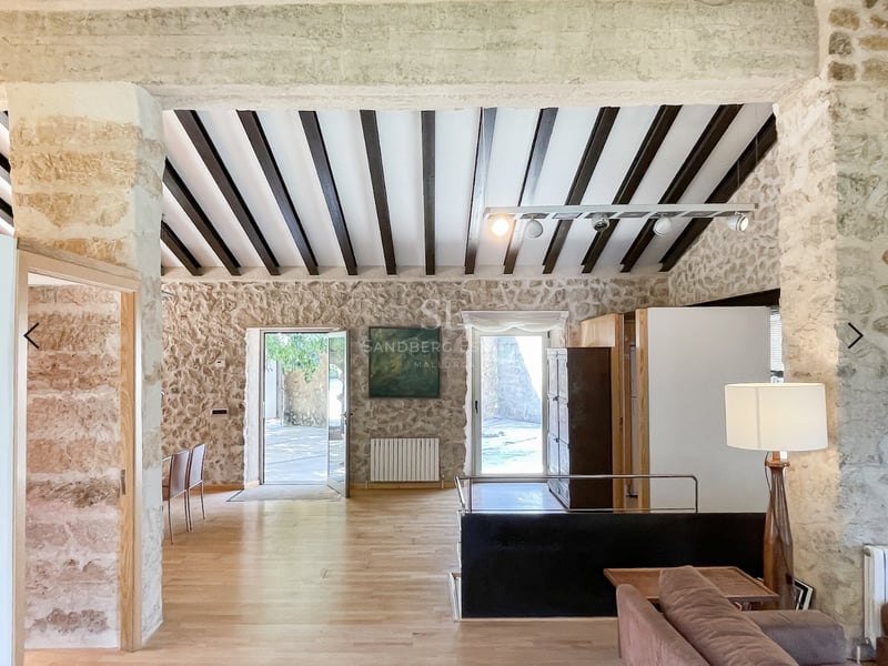 Salon à aire ouverte avec murs en pierre, poutres foncées au plafond et parquet en chêne clair.