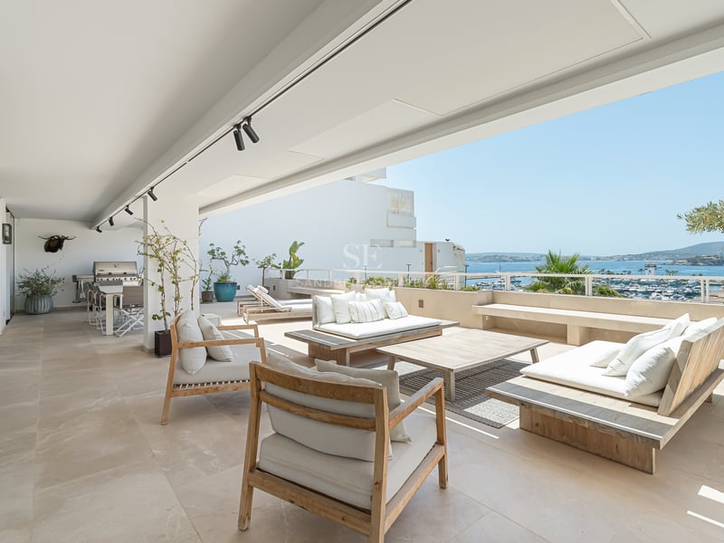 Grande terrasse blanche avec mobilier en bois donnant sur un port de plaisance et la mer Méditerranée.