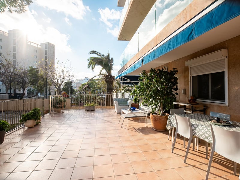 Grande terrasse extérieure avec carrelage en terre cuite, table à manger, salon de jardin et stores bleus.