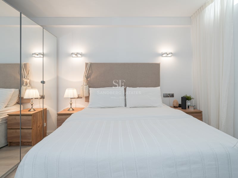 Une chambre moderne et lumineuse avec une tête de lit en beige, du linge blanc et de grands placards à miroirs.