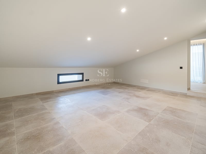 Pièce mansardée vide avec carrelage beige, plafond blanc incliné et spots encastrés.
