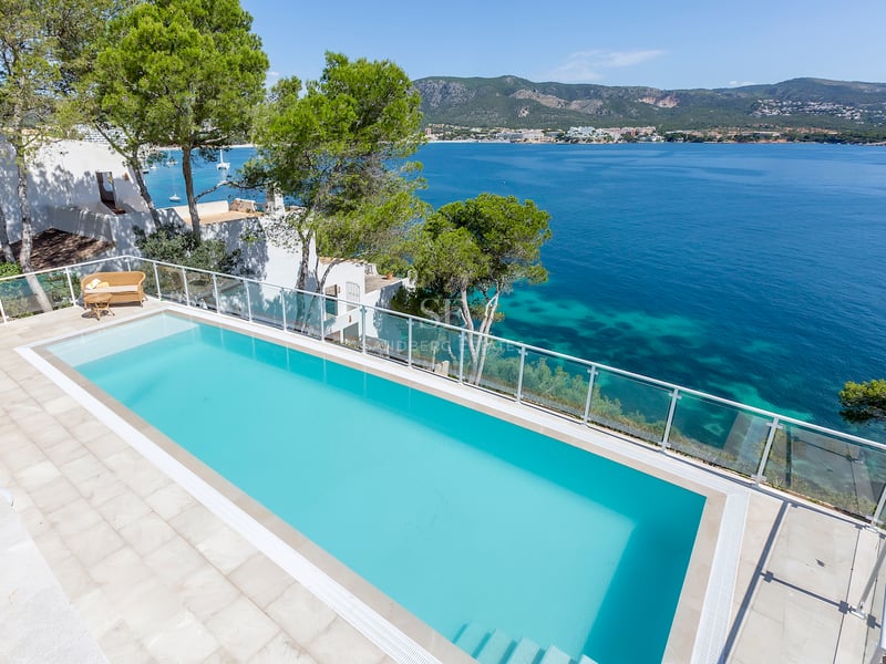 Vue en hauteur d'une piscine à débordement turquoise surplombant la mer Méditerranée avec des montagnes.