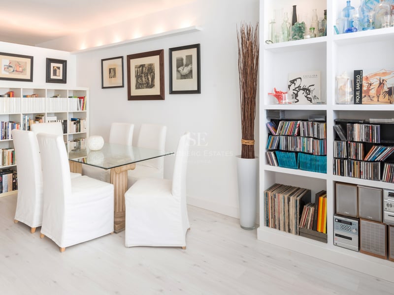 Une salle à manger lumineuse avec une table en verre, des chaises blanches et de grandes bibliothèques.