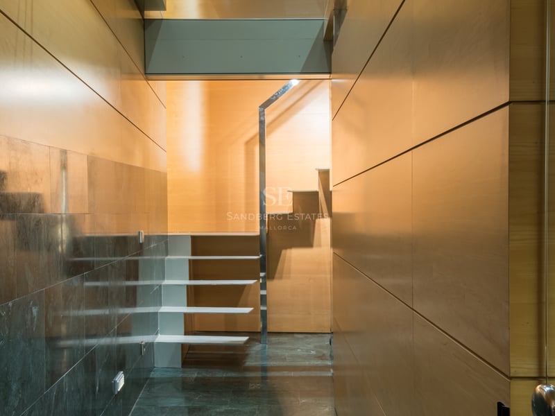 Modern interior hallway featuring light wood paneled walls, polished dark stone floors, and a white floating staircase.