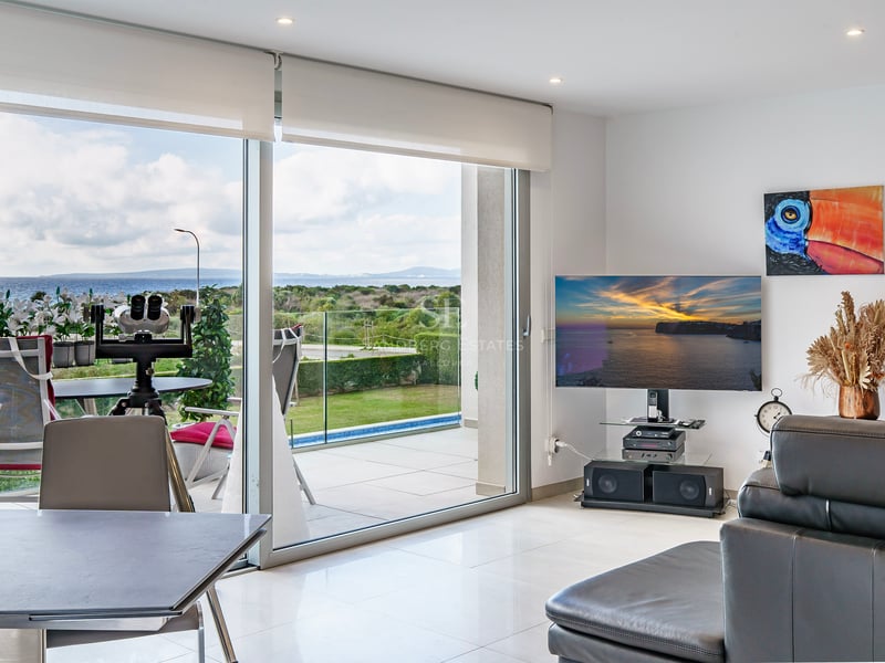 Salon lumineux avec grandes baies vitrées ouvrant sur terrasse avec vue mer, TV et canapé en cuir.