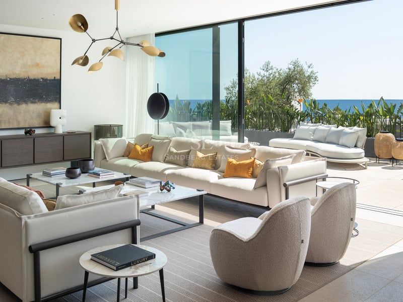 Grand salon contemporain avec canapés blancs, tables en marbre et baies vitrées s'ouvrant sur la mer Méditerranée.