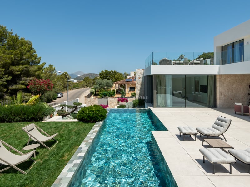 Villa de luxe blanche avec piscine à débordement, chaises longues sur terrasse en pierre et pelouse verte.