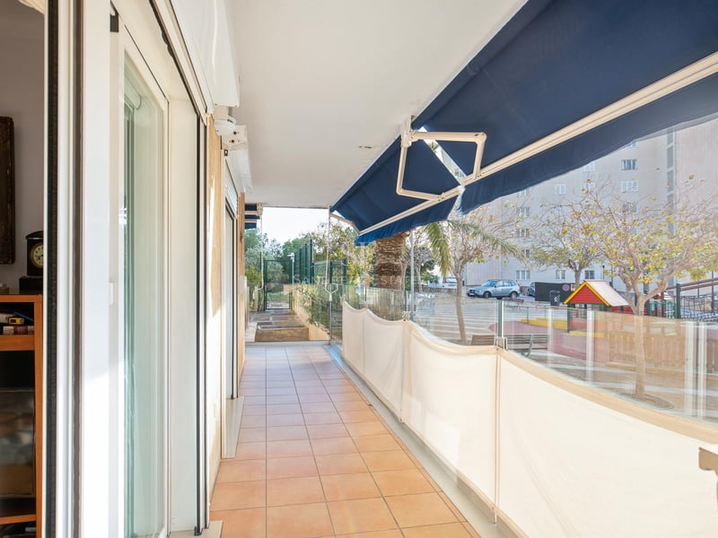 Long balcon avec carrelage en terre cuite, garde-corps en verre et stores bleus escamotables.