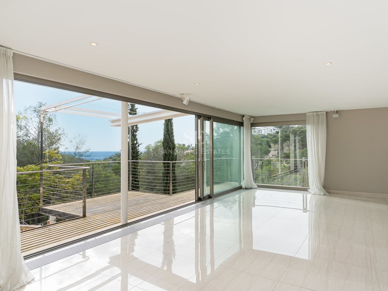 Salon moderne lumineux avec sols polis et baies vitrées coulissantes ouvrant sur une terrasse avec vue mer.