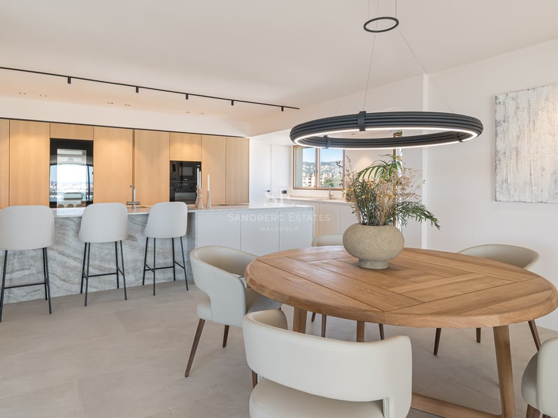Cuisine moderne avec îlot en marbre, tabourets blancs et table à manger circulaire en bois sous un luminaire suspendu.