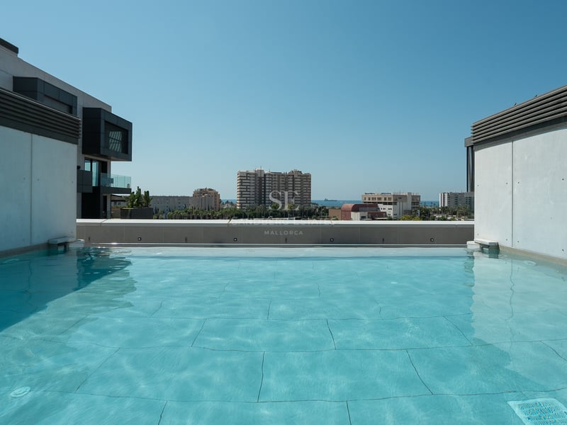 Grande piscine de toit turquoise avec architecture moderne en béton et vue lointaine sur la ville et la mer.