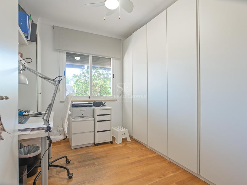 Pièce lumineuse avec de grands placards blancs, parquet en bois et un coin bureau près d'une fenêtre.