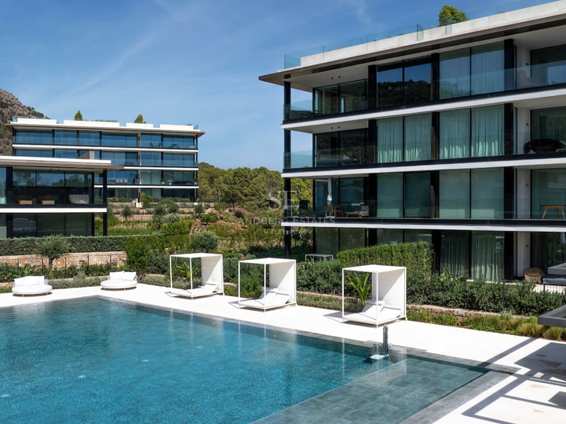 Piscine de luxe avec cabanas blanches devant un immeuble résidentiel contemporain en verre et cadre montagneux.