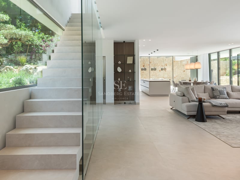 Espace de vie moderne avec escalier en pierre, garde-corps en verre et baies vitrées toute hauteur.