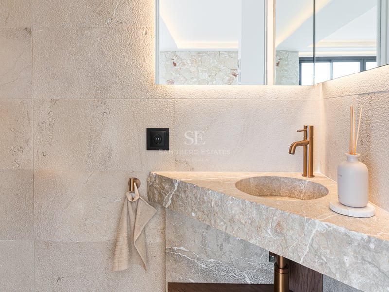 Gros plan d'un lavabo intégré en pierre naturelle avec robinetterie en laiton brossé et miroir rétroéclairé.