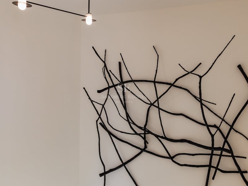Sculpture murale noire en forme de branches à côté d'un lustre moderne dans une pièce blanche avec escalier.