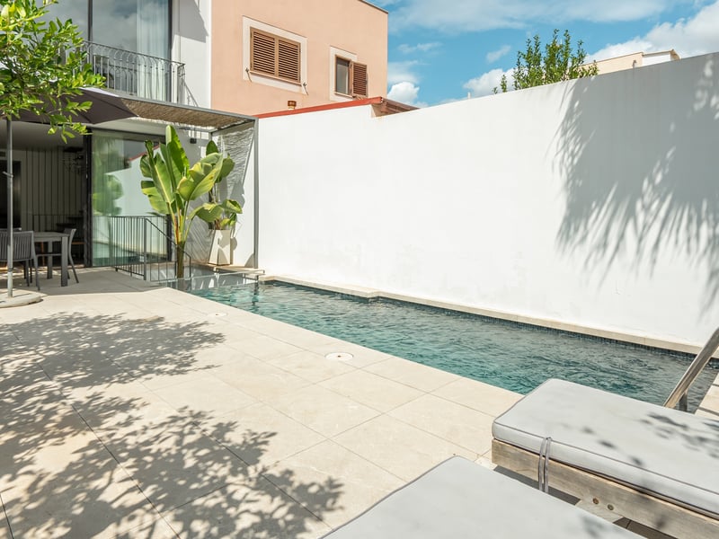 Une piscine étroite bleue sur une terrasse en dalles claires avec des chaises longues et un espace repas extérieur.