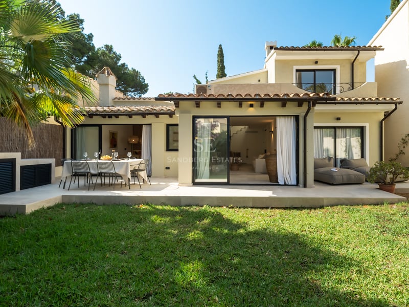 Façade arrière d'une villa crème avec pelouse, salle à manger extérieure et baies vitrées coulissantes.