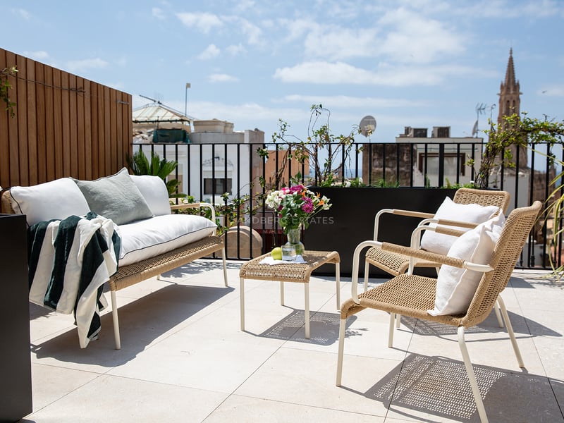 Terraza soleada en azotea con muebles de diseño, suelos de piedra clara y vistas al horizonte histórico de Palma.