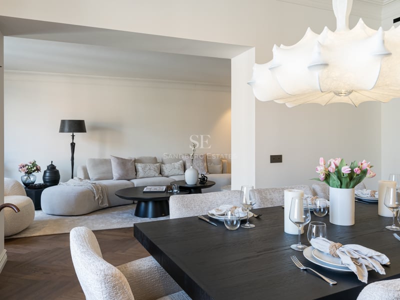 Elegant dark wood dining table set for guests, leading into a bright contemporary living room with herringbone floors.