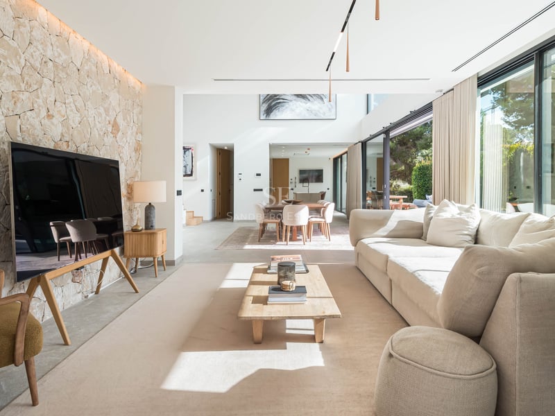 Salon spacieux avec un grand canapé crème, une table basse en bois et un mur d'accent en pierre naturelle claire.