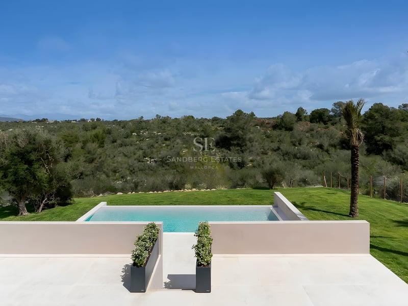 Vue surélevée d'une piscine à débordement avec terrasse en pierre claire dominant des collines verdoyantes.