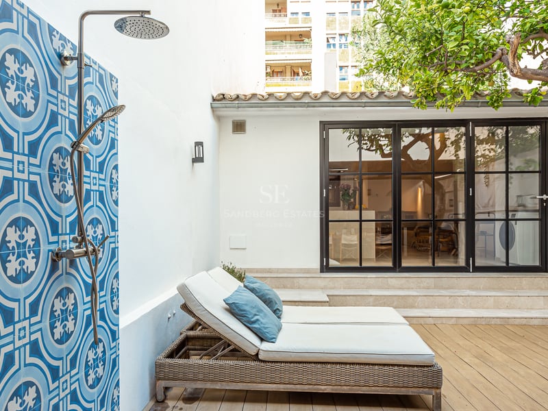 Douche extérieure avec carreaux bleus à motifs à côté de chaises longues sur une terrasse en bois avec un citronnier.