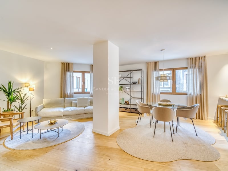 Salon spacieux à aire ouverte avec parquet en chêne clair, mobilier neutre et coin repas intégré.