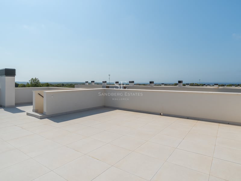 Terraza en la azotea con suelos de gres crema y muros blancos bajo un cielo azul despejado y vistas al mar.