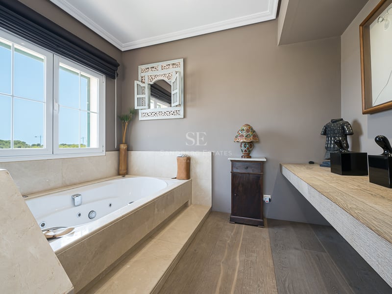 Salle de bain ensoleillée avec baignoire balnéo en marbre, parquet en bois et vue extérieure.
