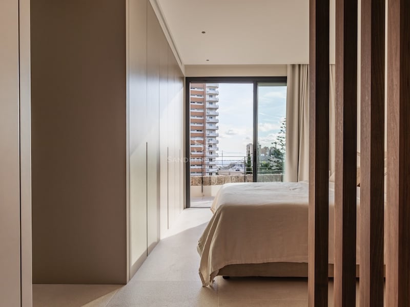 Chambre moderne avec placards intégrés, lit aux draps clairs et baie vitrée donnant sur la ville.