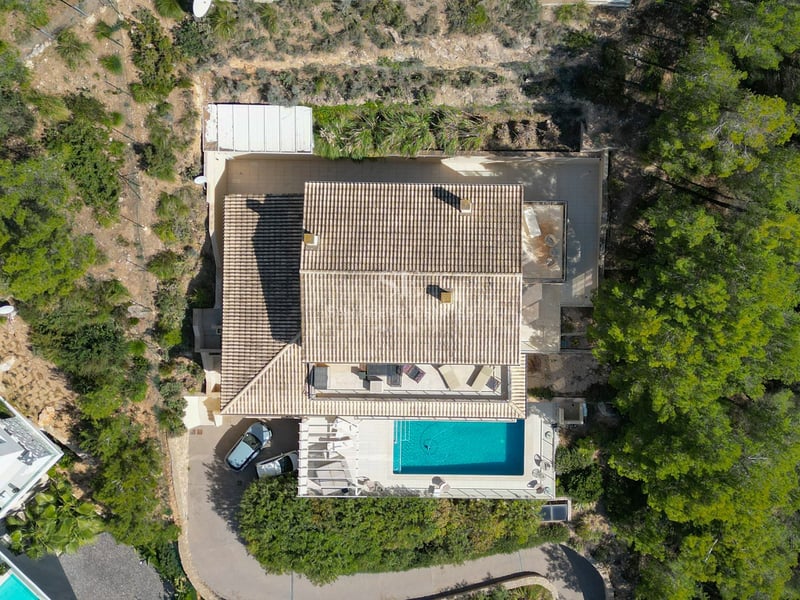 Vue aérienne d'une villa avec toit en tuiles, piscine et terrasses entourée d'une forêt de pins.