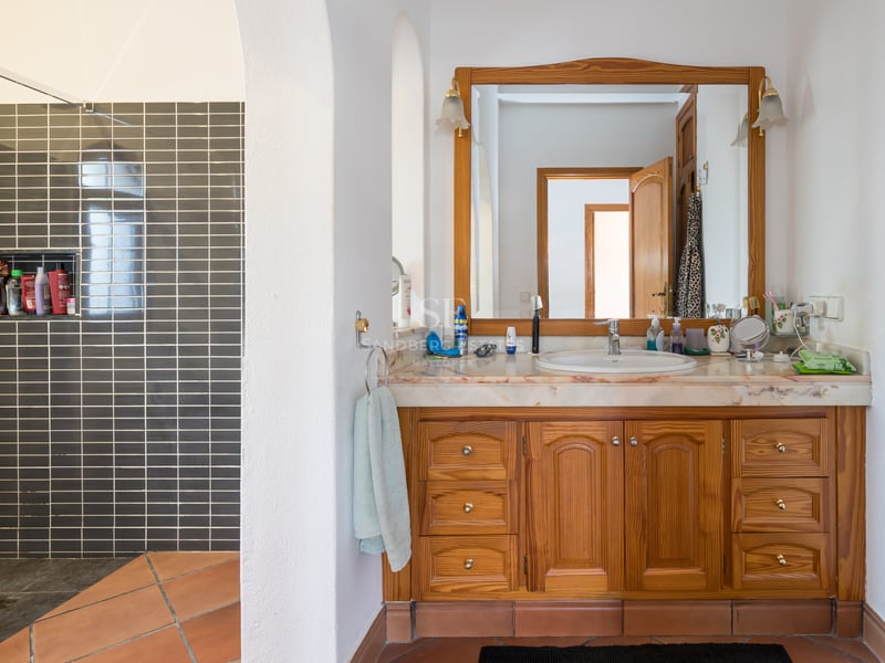 Salle de bain avec meuble en bois, plan en marbre, sol en terre cuite et douche à l'italienne grise.