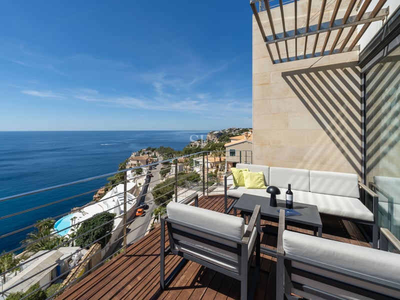 Terrasse en bois avec mobilier de salon gris et garde-corps en verre surplombant la mer Méditerranée.