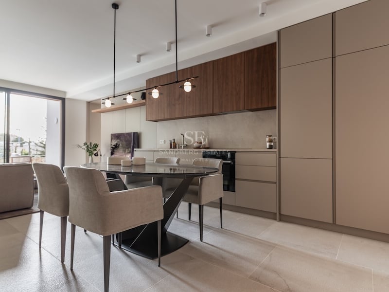 Salle à manger moderne avec table en marbre sombre, chaises beiges et cuisine minimaliste avec accents en bois.
