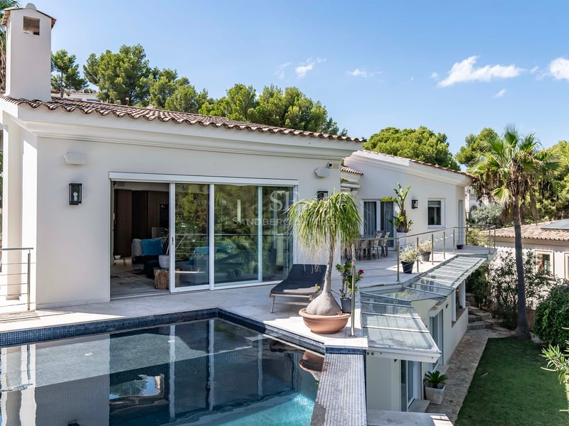 Vue en plongée d'une villa contemporaine blanche avec piscine carrelée sombre, terrasse vitrée et jardins luxuriants.