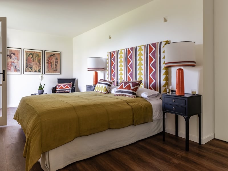 Chambre avec tête de lit géométrique, couvre-lit moutarde et lampes en céramique orange sur tables de chevet noires.