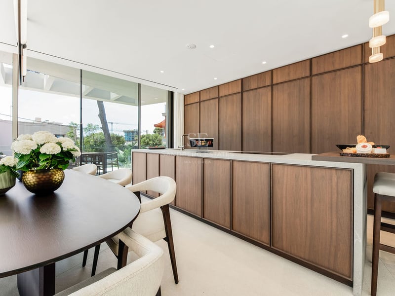 Cuisine moderne avec îlot central en bois sombre, plans de travail en pierre et coin repas près de grandes baies vitrées.