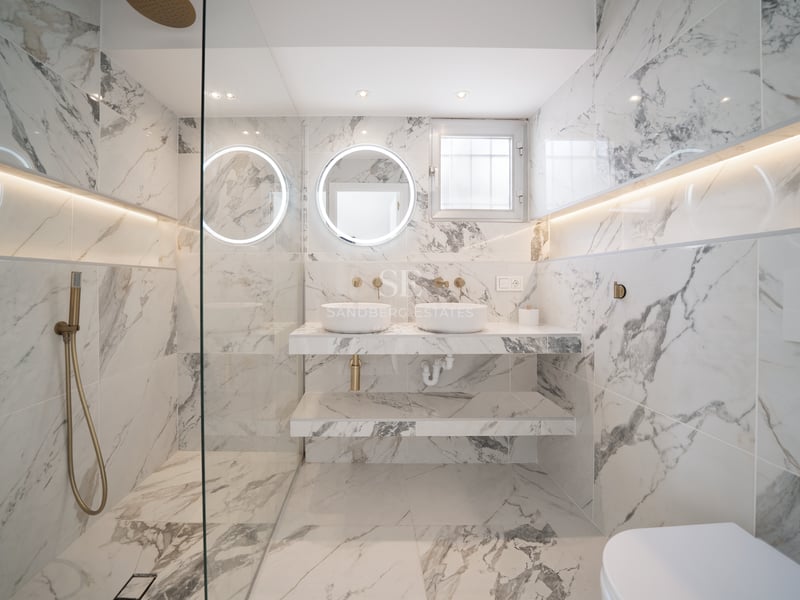 Salle de bains de luxe avec murs en marbre, double vasque, miroirs circulaires rétroéclairés et robinetterie en laiton.