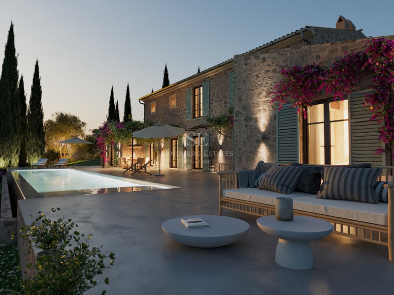 Villa en pierre au crépuscule avec piscine éclairée, mobilier de terrasse moderne et cyprès sous un ciel du soir.