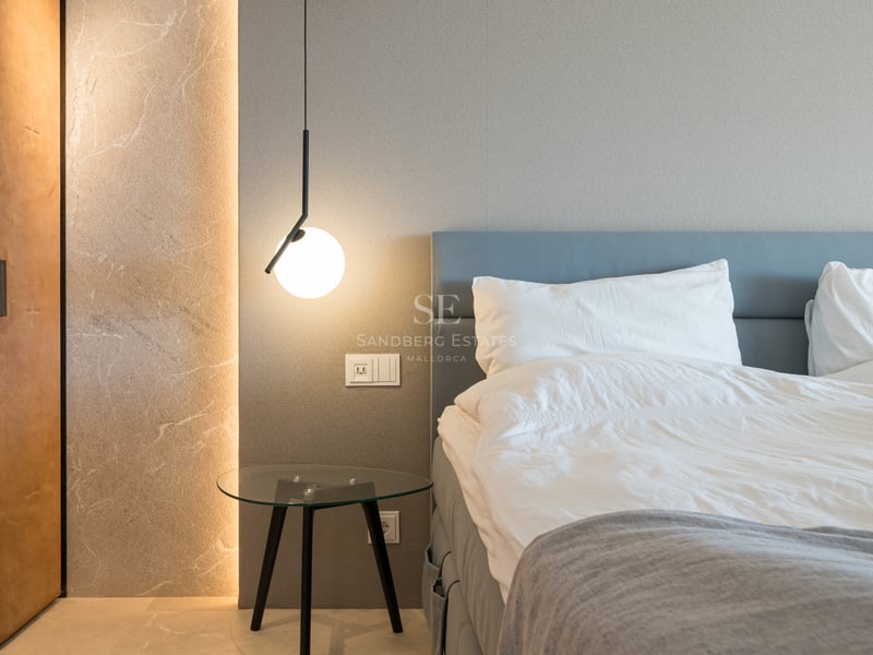 Chambre luxueuse avec tête de lit bleue, table en verre, suspension moderne et mur en pierre éclairé.