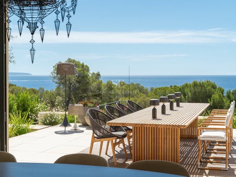 Table à manger extérieure en bois sur une terrasse surplombant une forêt de pins et la mer Méditerranée.