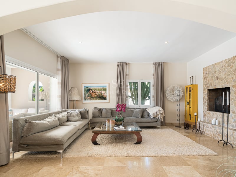 Salon spacieux avec canapés gris, tapis beige et un grand mur de cheminée en pierre naturelle.