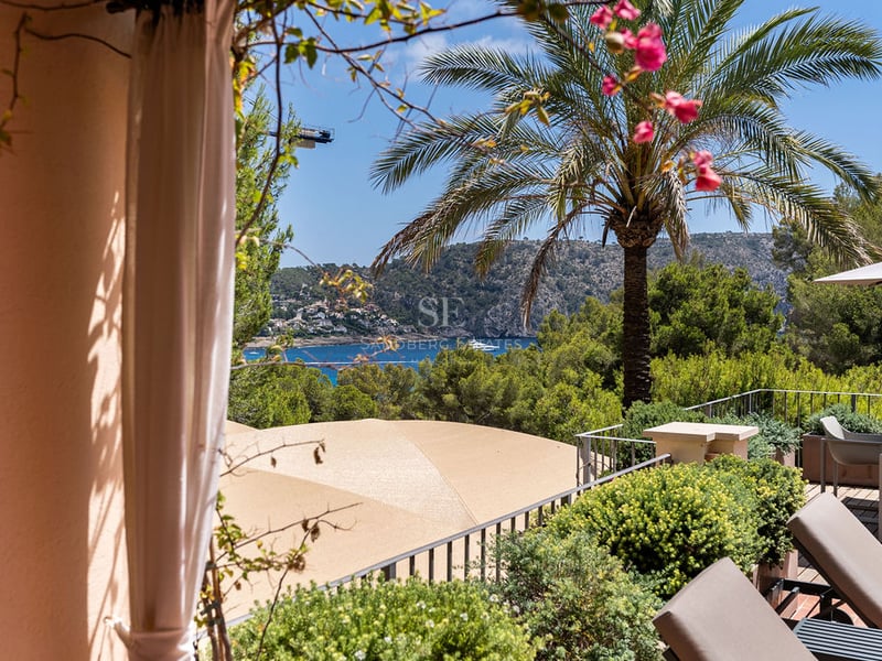 Terrasse avec chaises longues et coin repas offrant une vue sur une baie bleue et des montagnes verdoyantes.