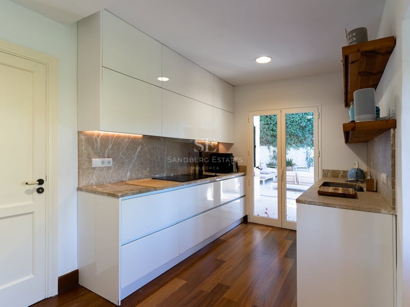 Cuisine moderne blanche avec plans de travail en marbre, parquet et portes vitrées ouvrant sur une terrasse.