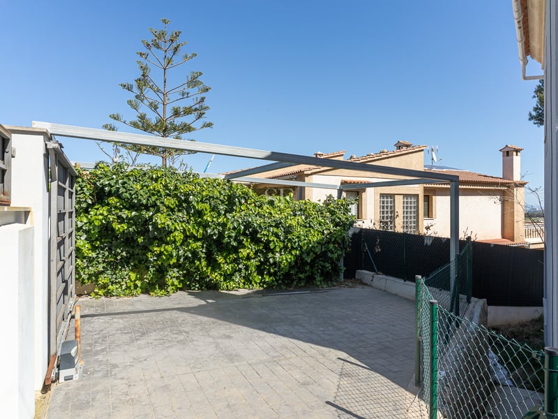 Espace de stationnement pavé avec portail coulissant automatique et structure métallique de pergola.