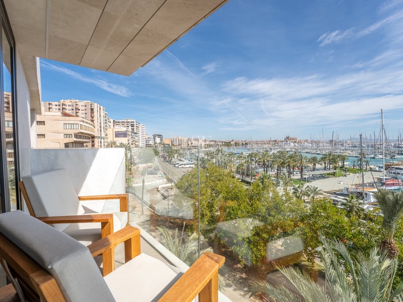 Balcon moderne avec fauteuils en bois et garde-corps en verre offrant une vue panoramique sur un port de plaisance.