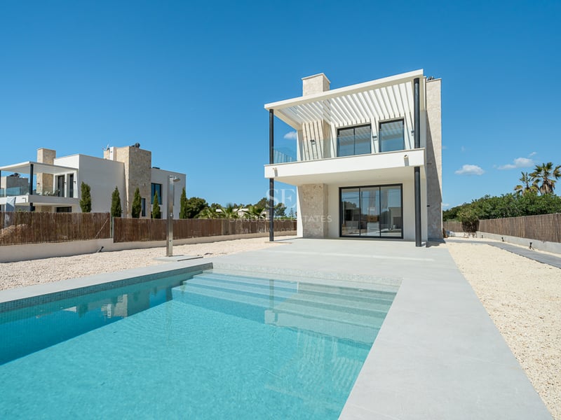 Piscine d'un bleu limpide avec marches, à côté d'une villa moderne de deux étages en blanc et pierre sous un ciel bleu.